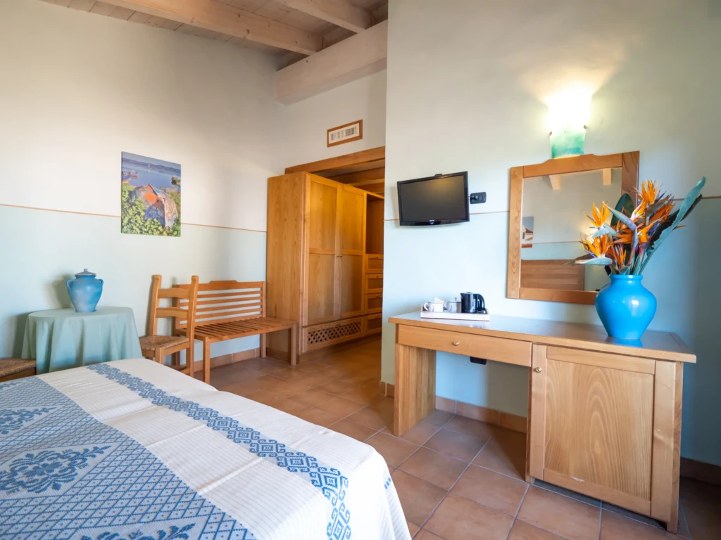 Camera matrimoniale con letto, scrivania in legno, specchio e TV all'Hotel Luci del Faro