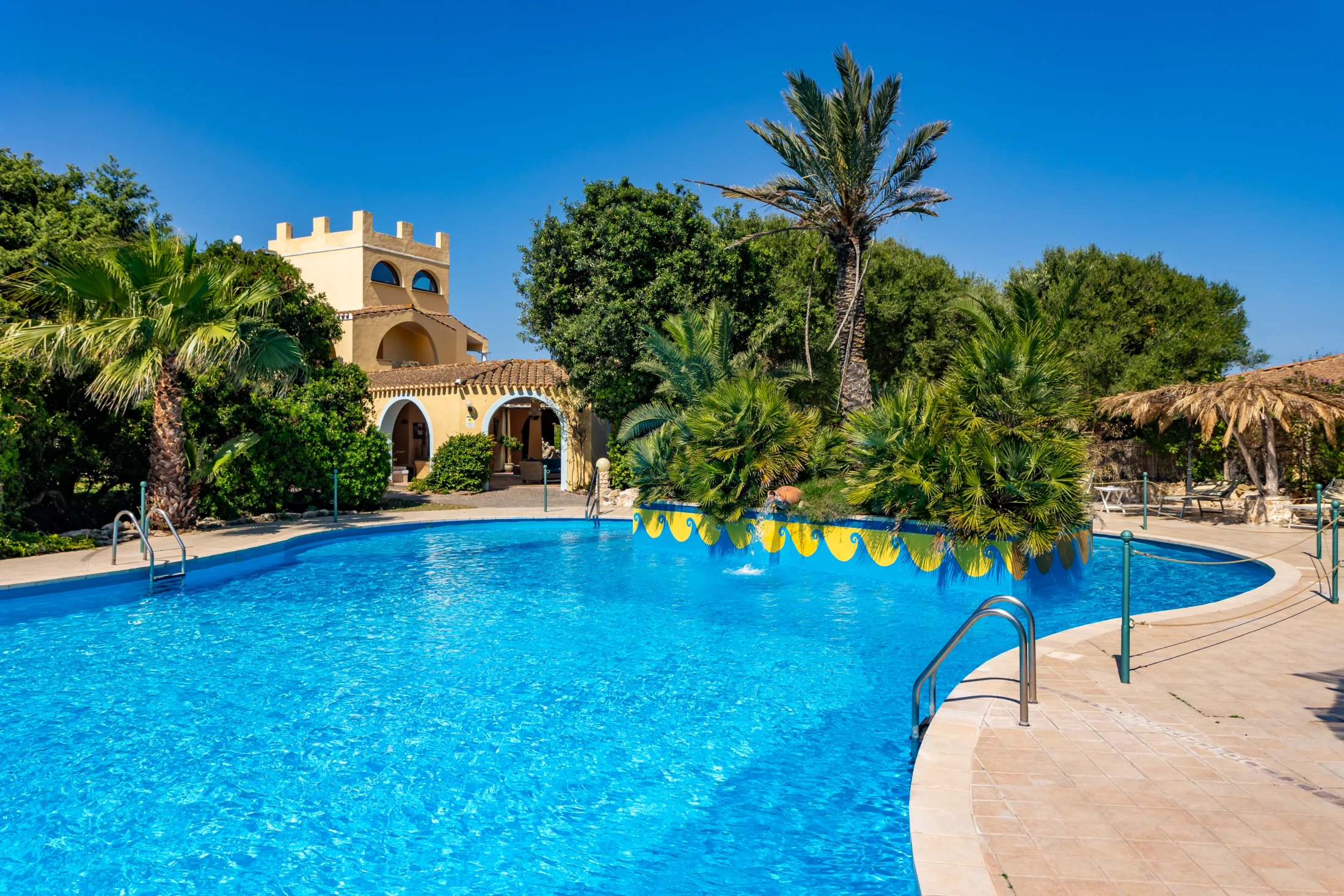 Piscina esterna con acqua blu circondata da palme e vegetazione mediterranea all'Hotel Luci del Faro