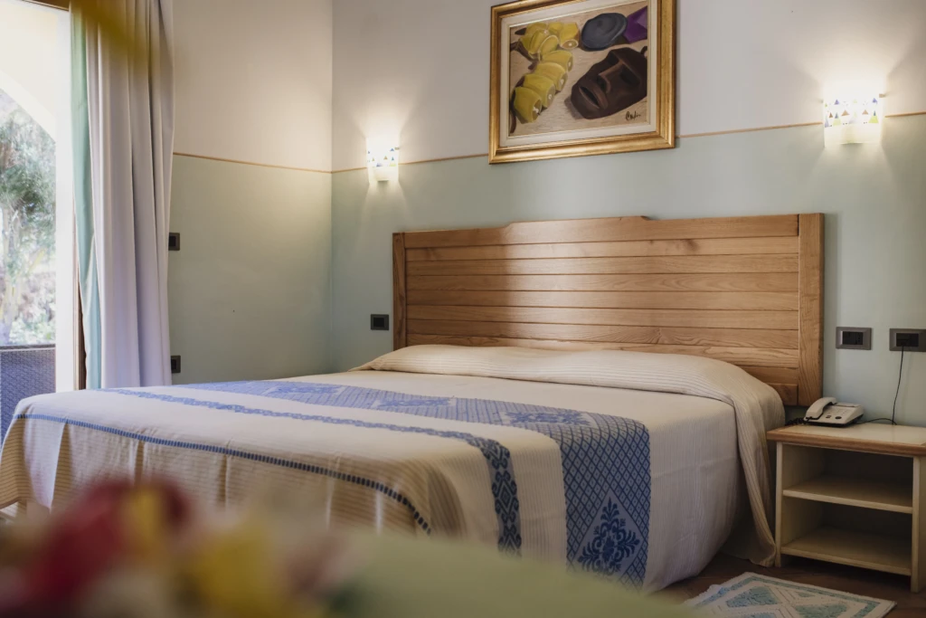 Camera matrimoniale con letto king size, testiera in legno, comodini e quadro decorativo all'Hotel Luci del Faro
