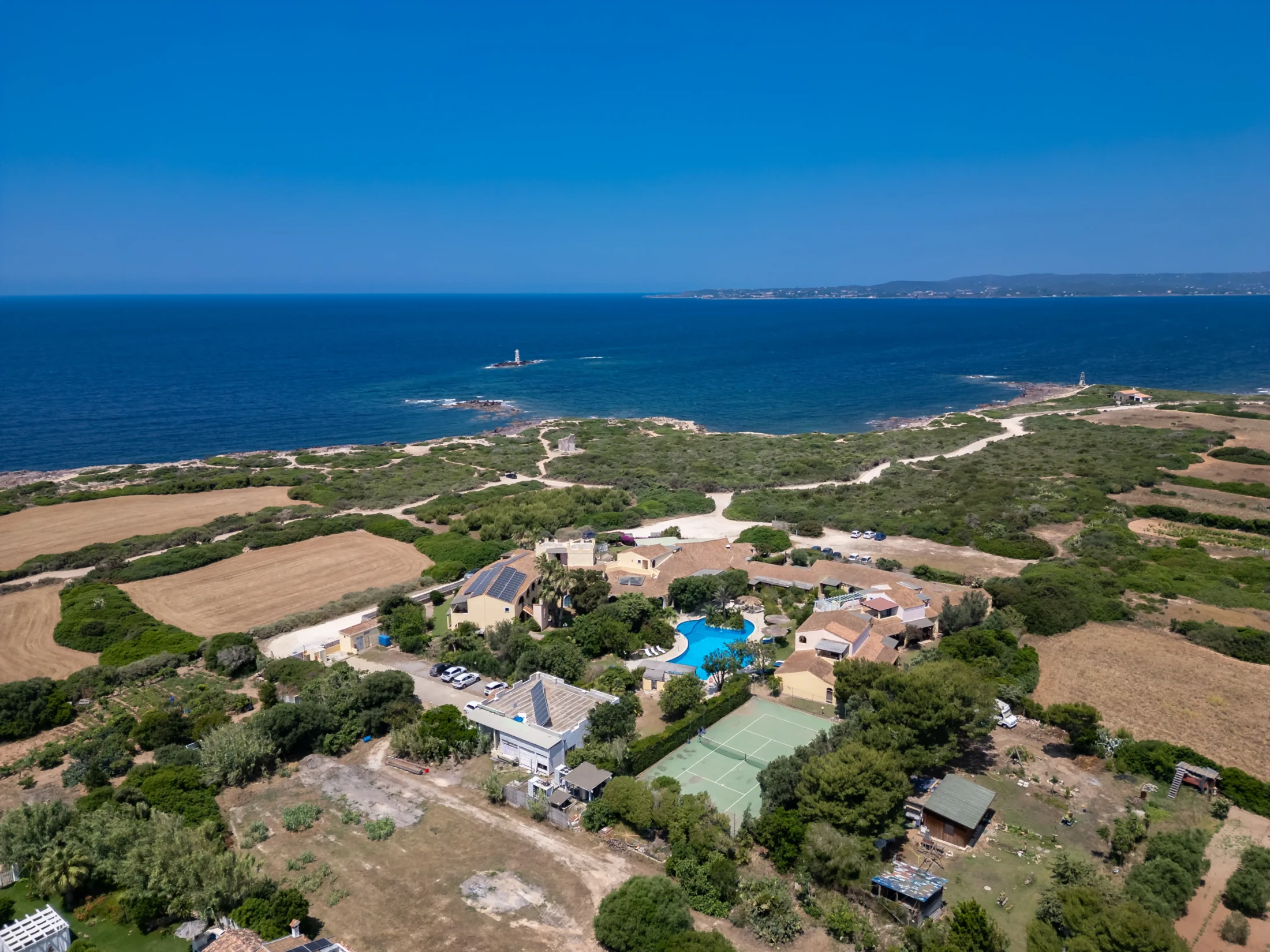 Luftaufnahme des Hotel Luci del Faro mit Pool umgeben von mediterraner Vegetation und Meerblick auf Calasetta, Sardinien