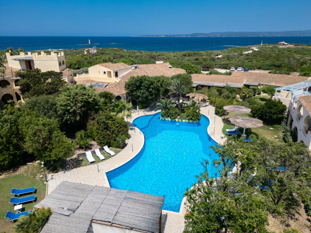 Vista aerea della piscina a forma libera dell'Hotel Luci del Faro con mare azzurro sullo sfondo a Calasetta