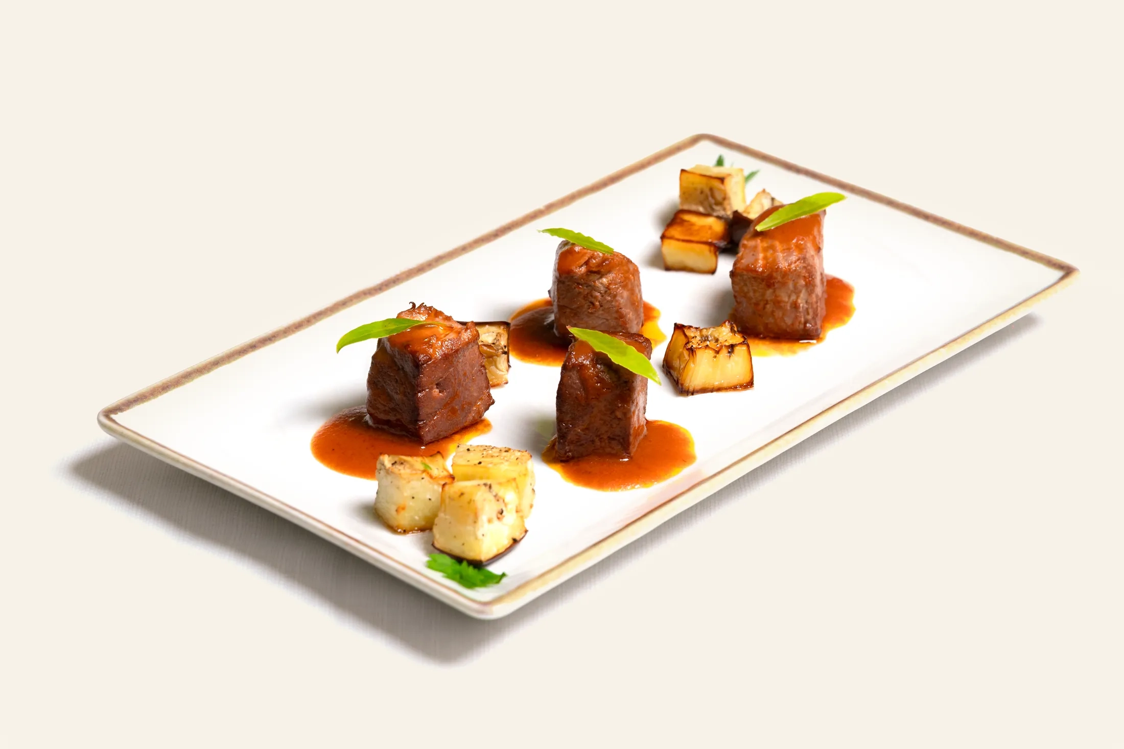 Piatto gourmet con bocconcini di carne glassata, verdure grigliate e salsa su piatto bianco rettangolare