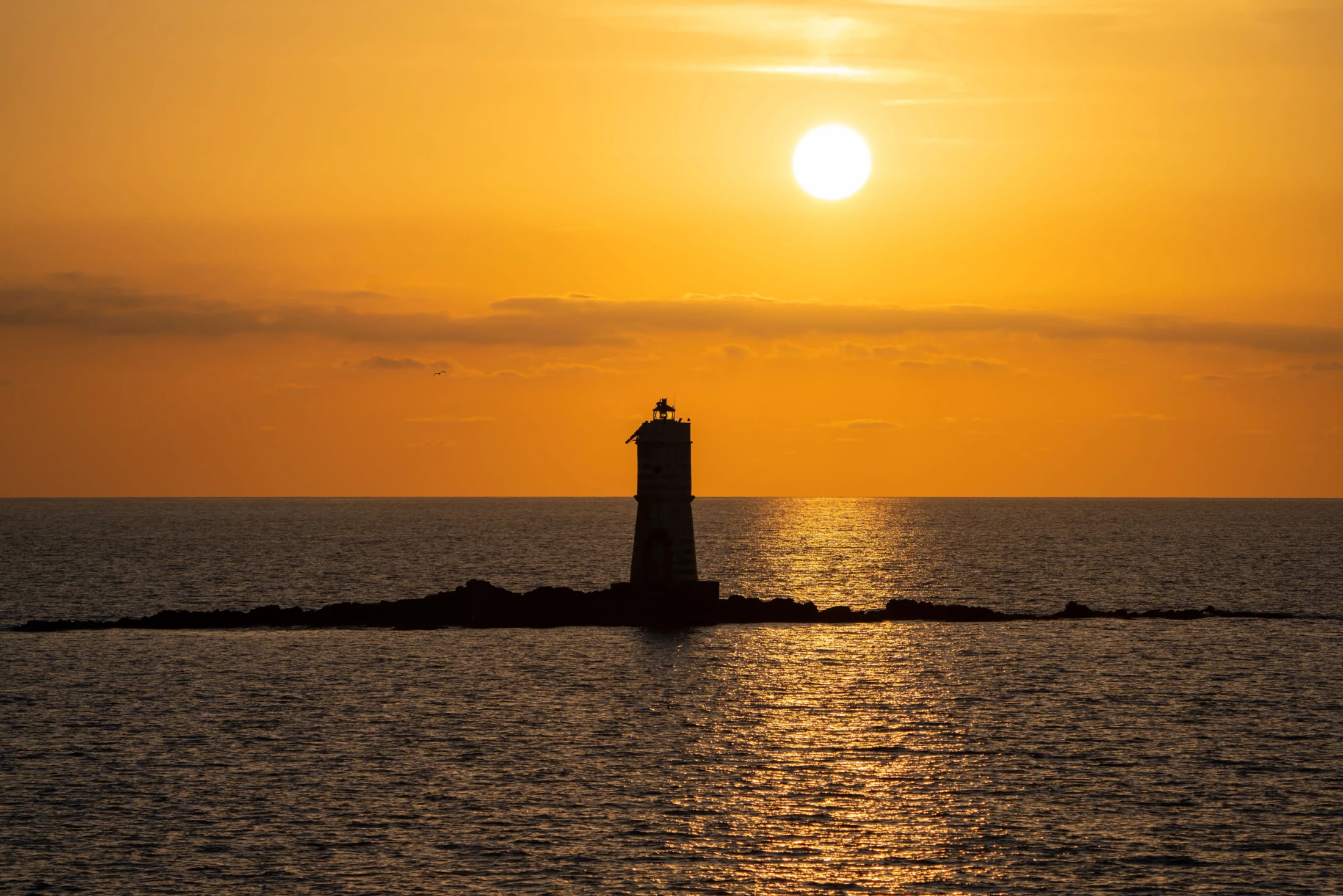 Tramonto dorato sul faro di Calasetta con mare calmo e cielo arancione