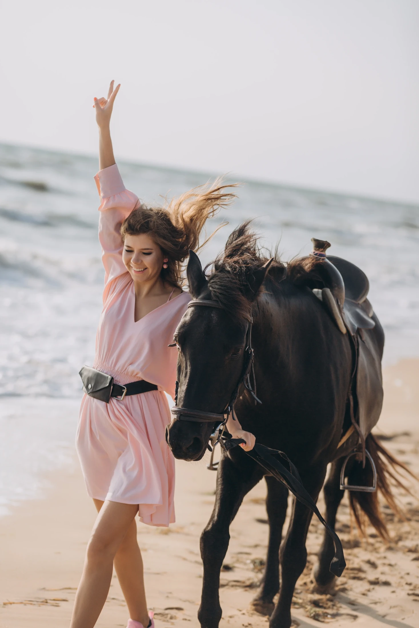 Donna in abito rosa che danza sulla spiaggia accanto a un bufalo nero con il mare sullo sfondo