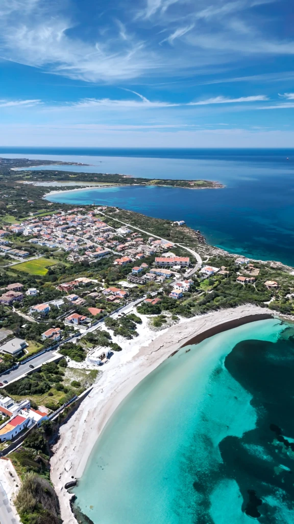 Vista aerea di spiaggia con sabbia bianca, acque turchesi cristalline e costa urbana affacciata sul mare