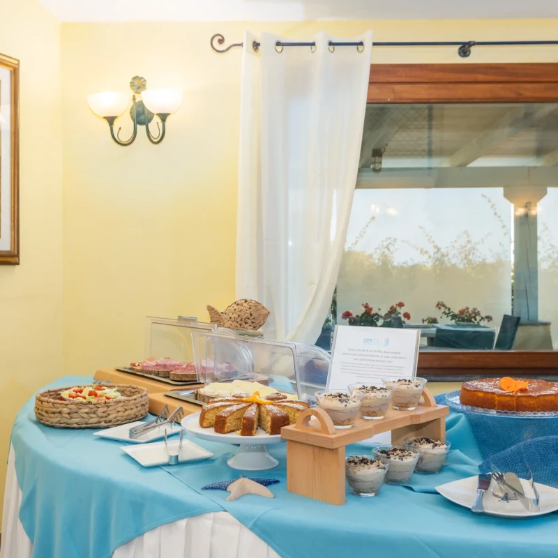 Buffet colazione Hotel Luci del Faro con tavolo imbandito di dolci e prodotti da forno davanti a finestra con vista giardino