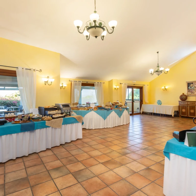 Sala colazione dell'Hotel Luci del Faro con buffet, tavoli apparecchiati e pareti gialle in stile mediterraneo