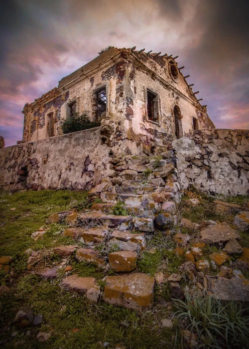 Rovine di edificio storico in pietra a Calasetta al tramonto con cielo drammatico rosa e arancione