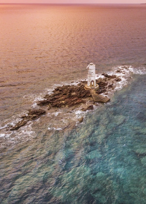 Faro bianco su scogliera circondata da acque turchesi al tramonto a Calasetta, Sardegna