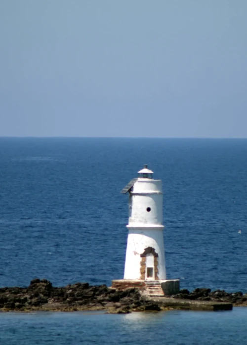 Faro bianco su scogliera con barca a vela nel mare blu di Calasetta