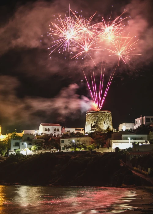 Fuochi d'artificio notturni sul borgo marinaro di Calasetta illuminato, con riflessi sul mare