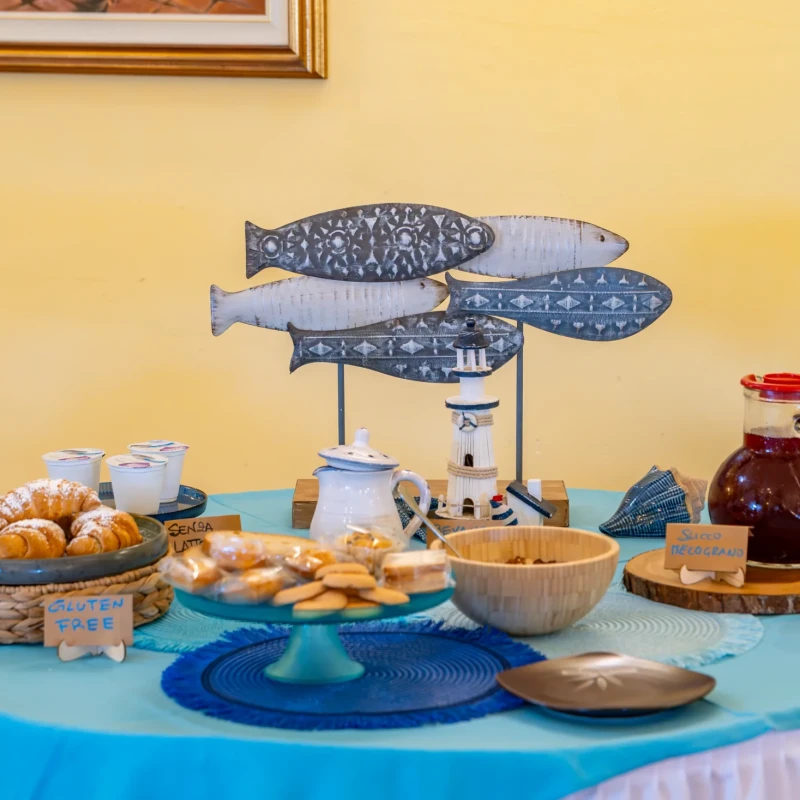 Buffet colazione con croissants, biscotti, marmellata e vassoi di ceramica blu su tavolo con tovaglia azzurra all'Hotel Luci del Faro