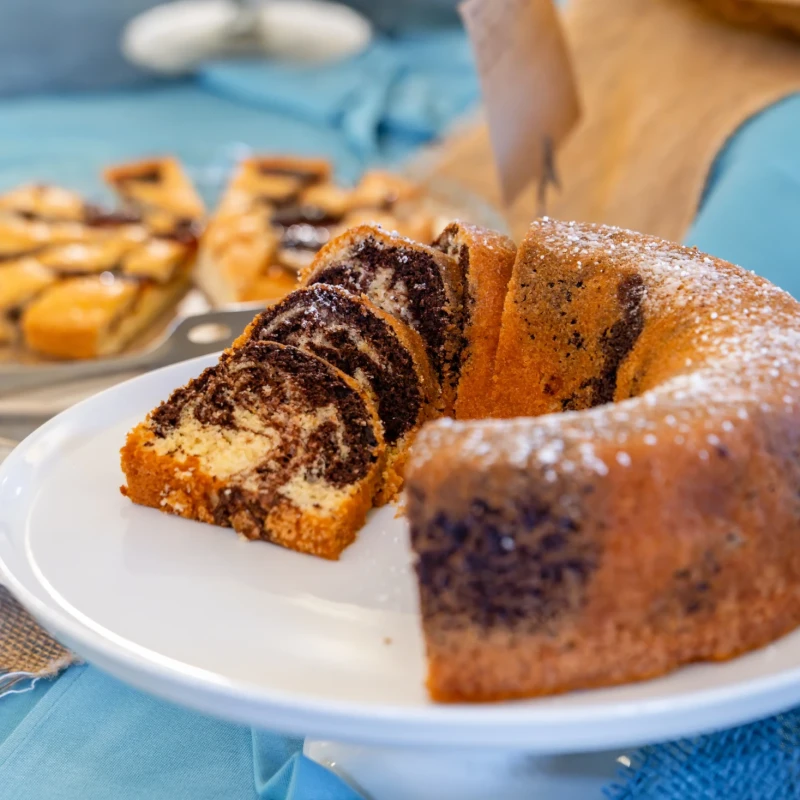 Buffet colazione con ciambella al cioccolato, biscotti e dolci su piatti bianchi all'Hotel Luci del Faro di Calasetta