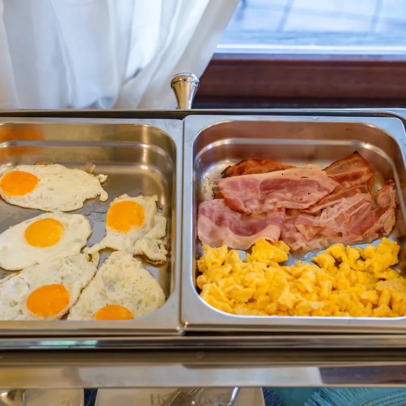 Buffet colazione con uova fritte, bacon croccante e mais dolce in vaschette riscaldate Hotel Luci del Faro