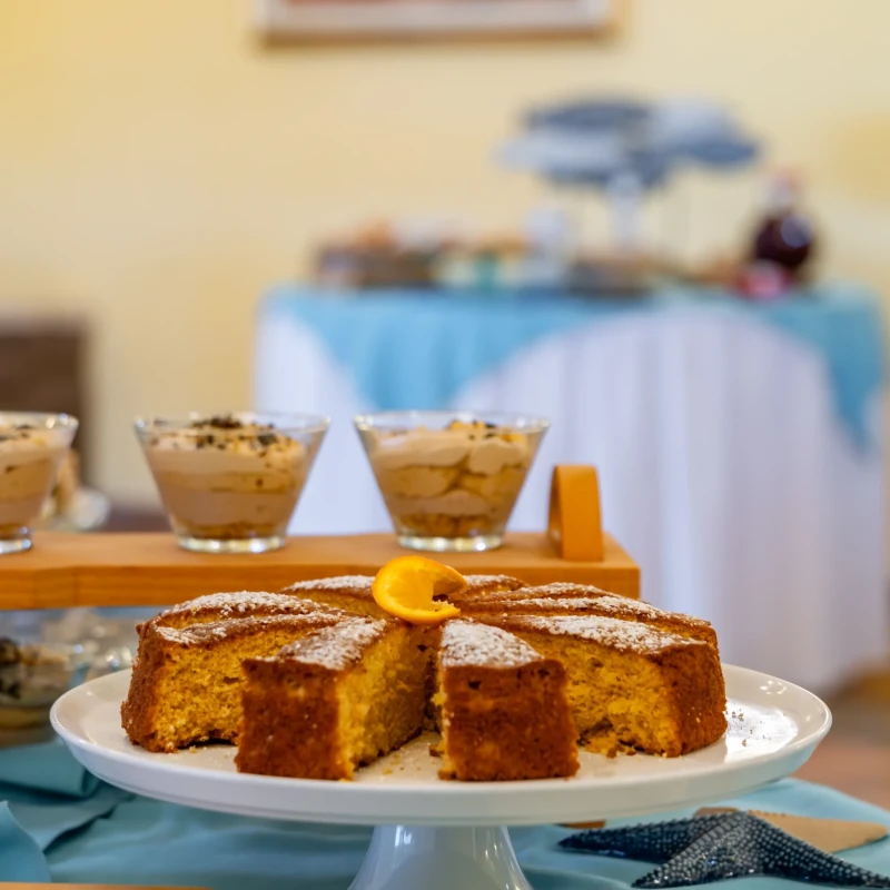 Buffet di dolci con torta a fette in primo piano e piscina sullo sfondo all'Hotel Luci del Faro Calasetta