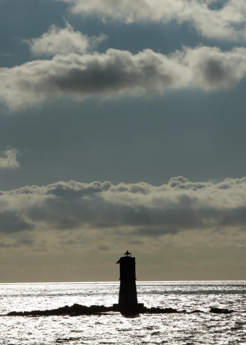 Faro solitario in mare al tramonto con cielo nuvoloso drammatico a Calasetta