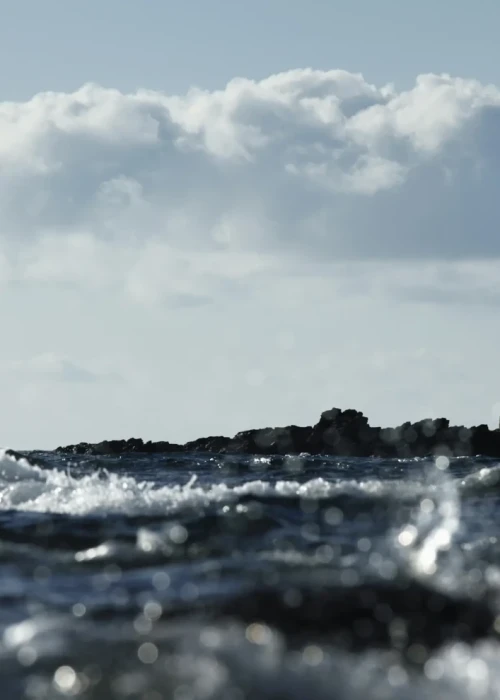 Faro con barca a vela sullo sfondo del mare mosso di Calasetta