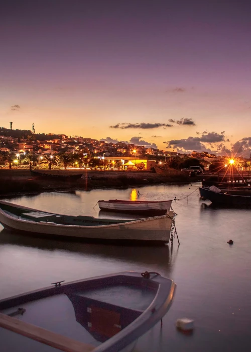 Barche da pesca ormeggiate al tramonto nel porto di Calasetta con luci del paese sullo sfondo