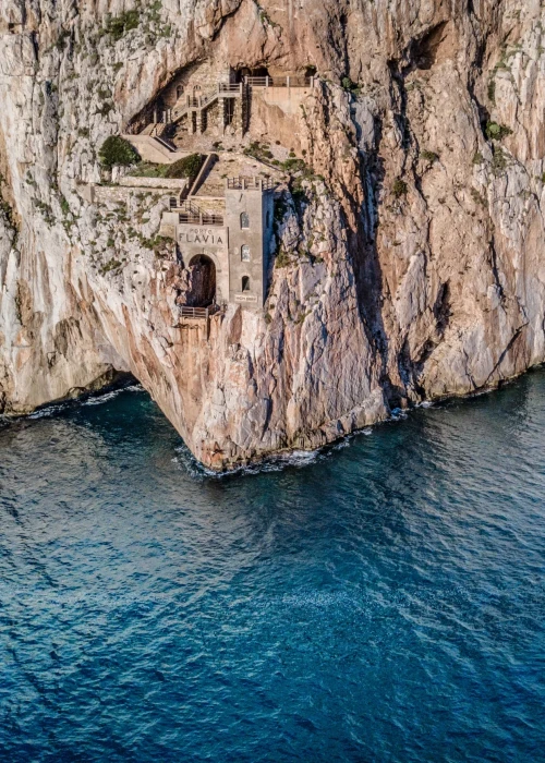 Scogliere calcaree a picco sul mare cristallino turchese della costa sarda vicino a Calasetta